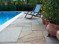 Warme Farbtöne für ein harmonisches Gesamtbild! Liegestuhl und mediterrane Pflanzen auf Natursteinplatten aus hellem Sandstein direkt am Pool