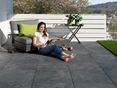 Junge Frau liest auf Terrasse mit dunklen Feinsteinzeugplatten in Schieferoptik und modernen Möbeln