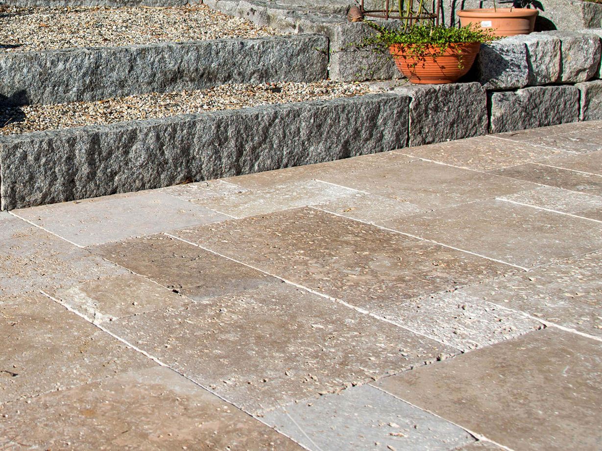 Terrasse mit Natursteinplatten aus braunem Travertin, im Hintergrund eine Treppe mit Granitsteinen