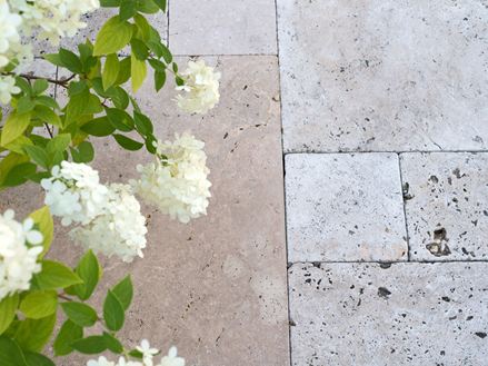Beige Travertinplatten im Römischen Verband verlegt mit weißen Blumen von oben