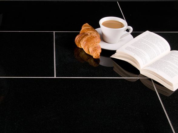Dunkle Granit-Fliesen Nero Assoluto mit Croissant, Kaffeetasse und einem aufgeschlagenen Buch