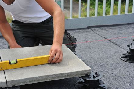 Platten werden auf Stelzlager verlegt, der Verleger nutzt eine Wasserwaage